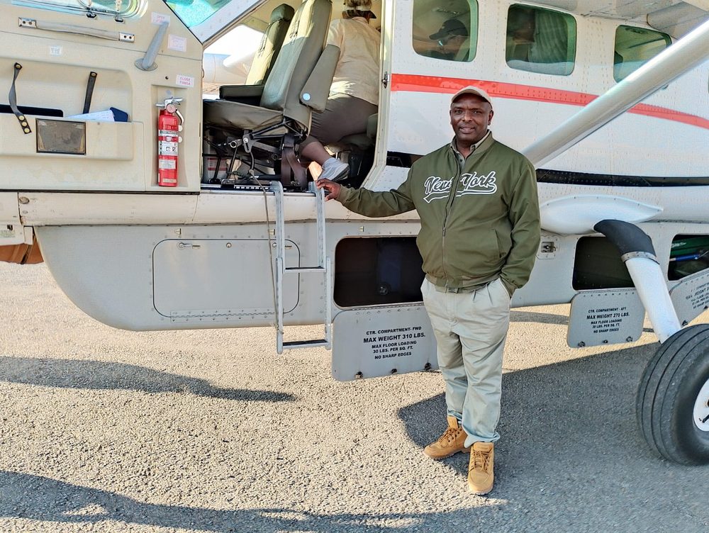 Our founder standing beside the open door of a single-engine bush plane on a gravel airstrip, one hand resting on the airframe.